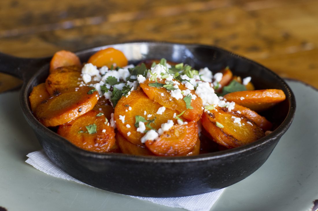 Roasted glazed carrots in a cast iron skillet, scattered with crumbled cheese and chopped herbs.