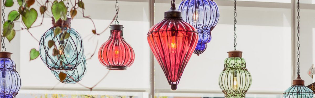Hand blown glass lanterns in ruby, cobalt, sea glass and olive hanging on chains, each lit by a warm filament bulb.